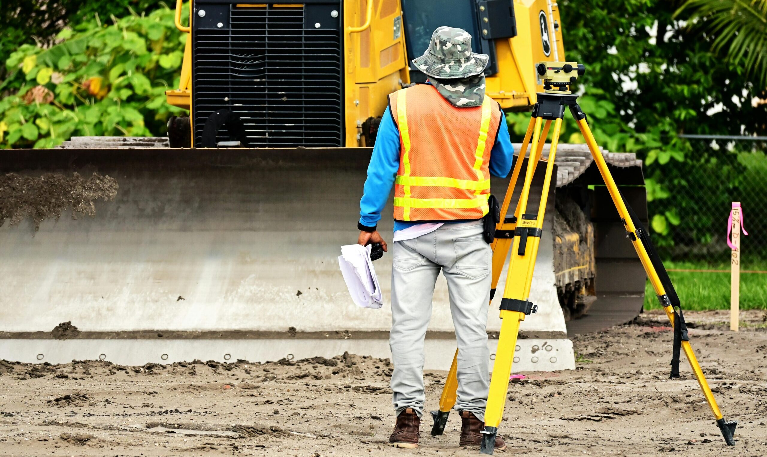 Surveyor with equipment at an active construction site, observing bulldozer operations.